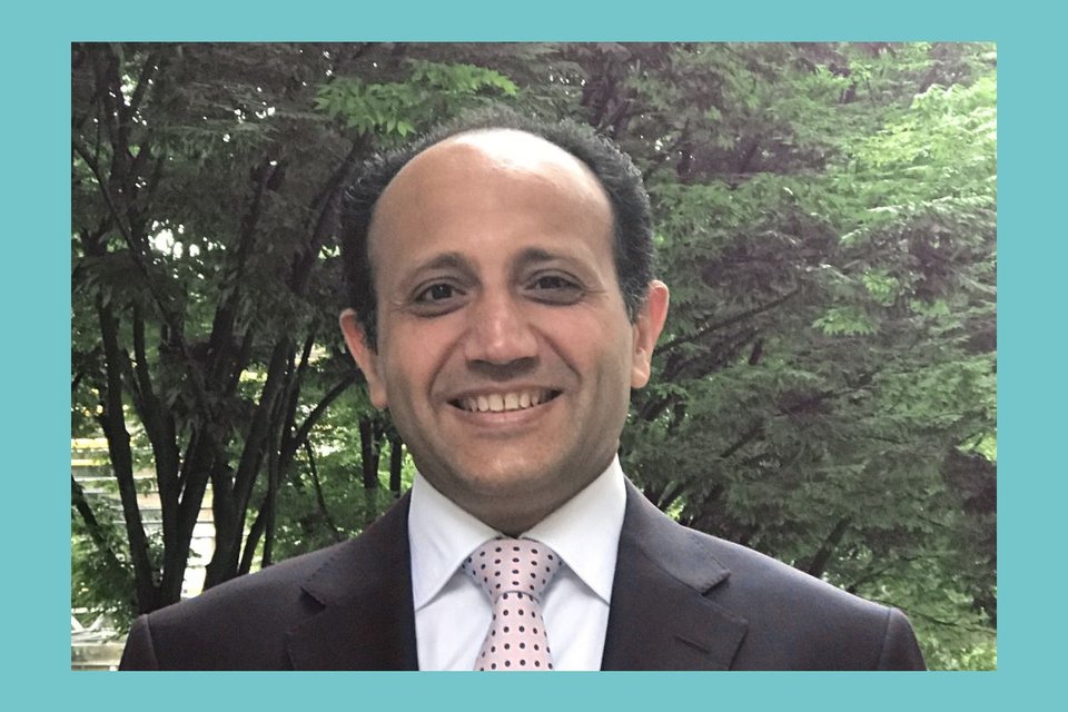 Dr Ahmed Ahmed smiling with trees in the background layered over a turquoise rectangle