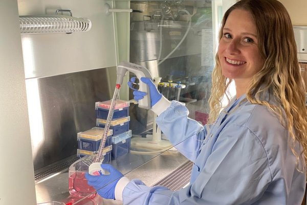 Image shows Dr Ashley Boyle wearing a white coat doing an experiment in a lab.