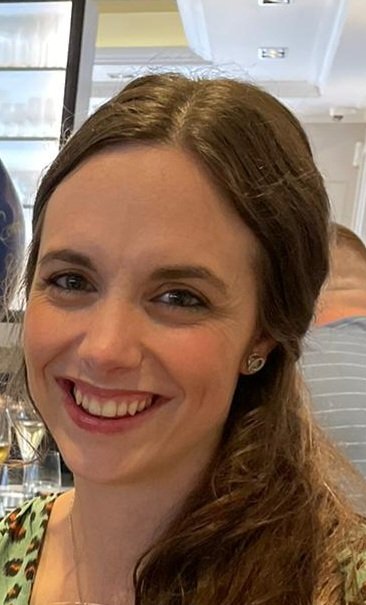 Dr Rachel Pounds, a white woman with long brown hair, looks at the camera, smiling