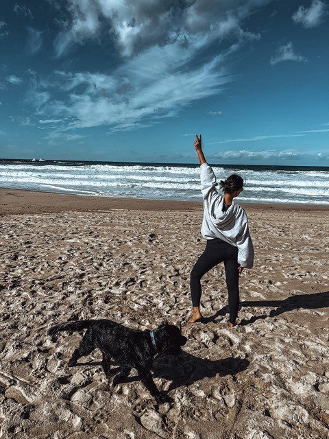 A women standing on a beach with a black dog next to her