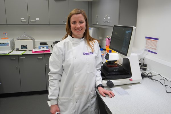 white woman with medium length straight red hair wearing a lab coat and smiling