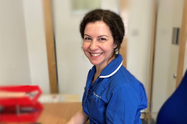 Midwife Michelle Anderson sitting at her desk in blue midwife uniform and smiling