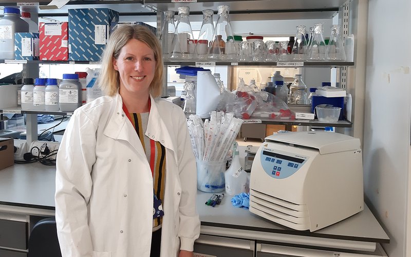 Image shows Dr Sarah Kitson in a white coat in a lab.