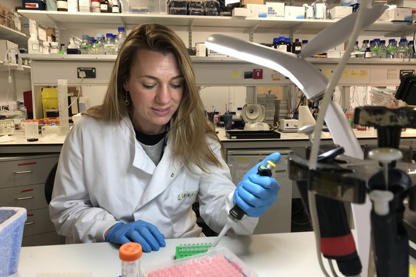 Image shows Dr Sarah McClelland, Senior Lecturer at Barts Cancer Institute, Queen Mary University of London in a lab. She's wearing a white coat and doing some lab tests.