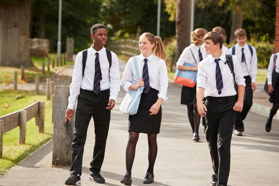 Three teenage school students, two boys and a girl, are walking chatting and laughing
