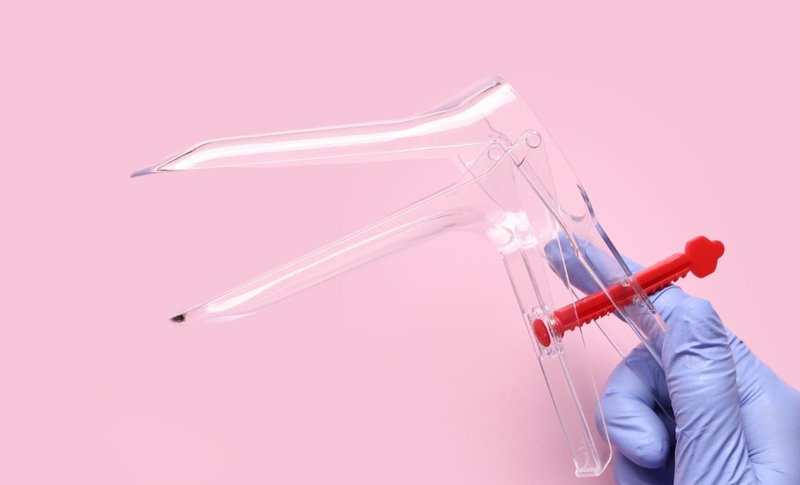 A hand with a blue rubber glove holds a speculum