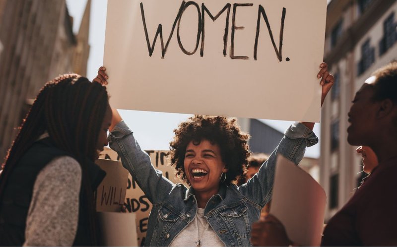 A Black woman holding a placard that says woman