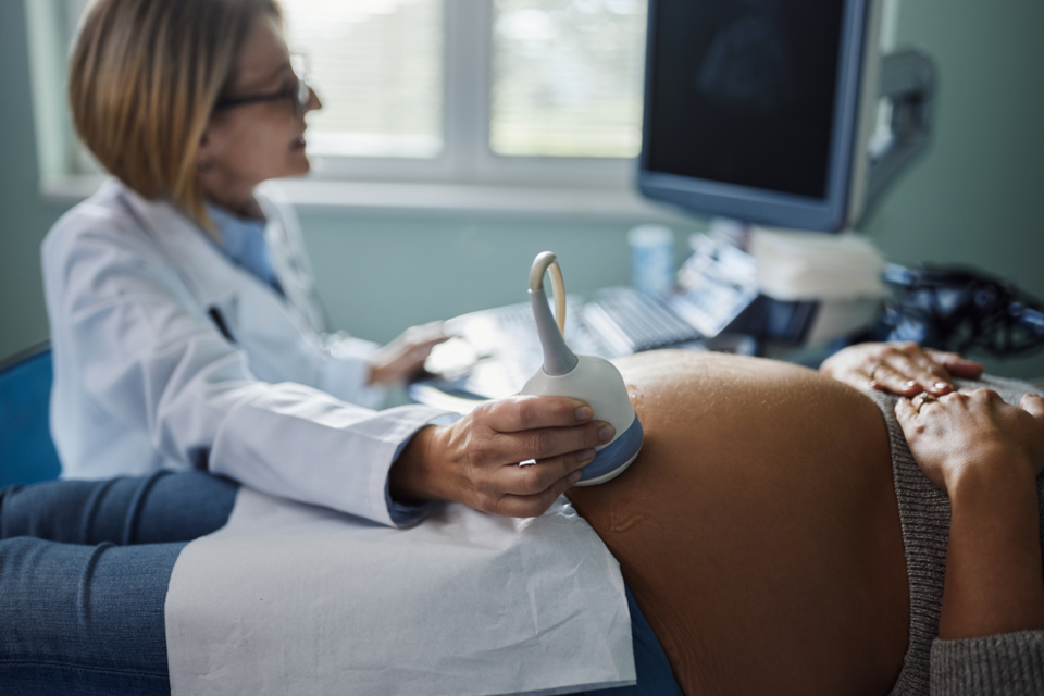Ultrasound being conducted on a late stage pregnancy, bump is large in foreground and healthcare professional is blurred in background